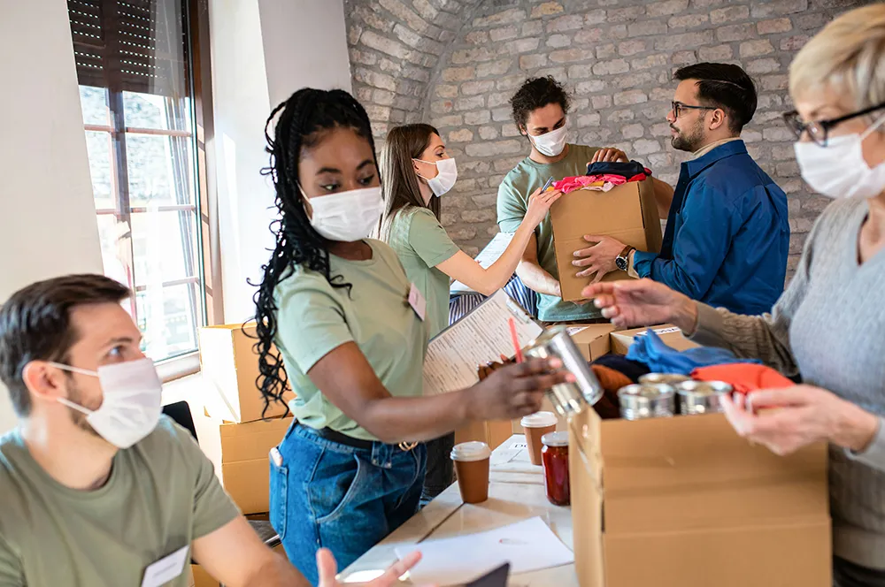 team of volunteers in face masks packing donation boxes together