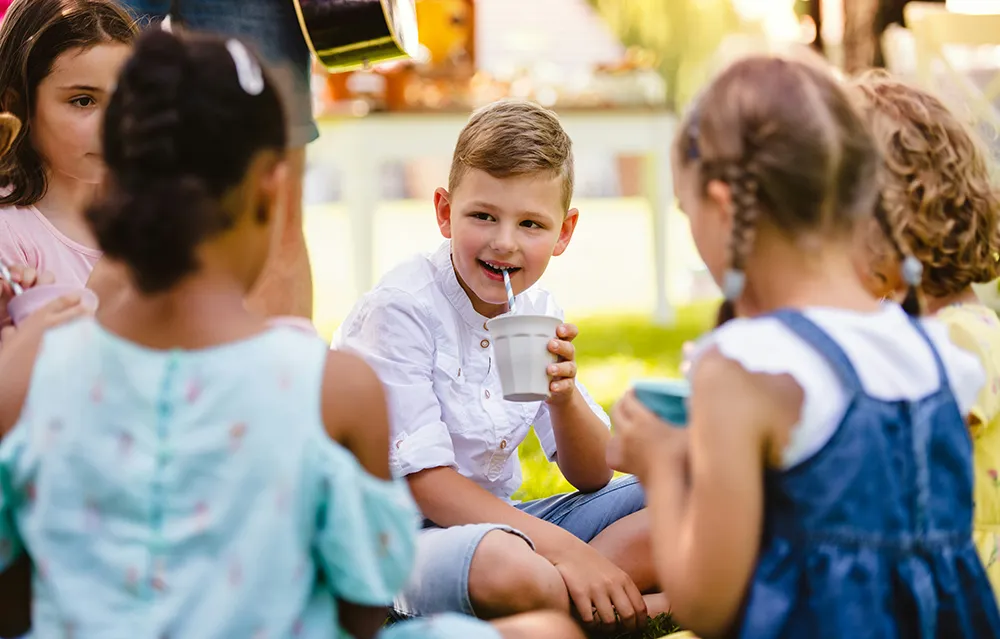 young children sitting together at a table, one drinking from a cup